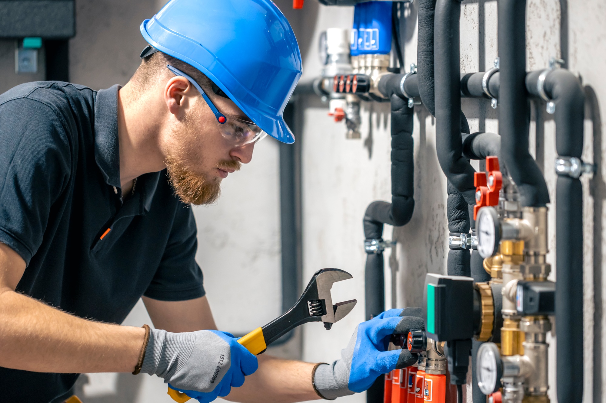 A man installs a heating system in a house and checks the pipes with a wrench.